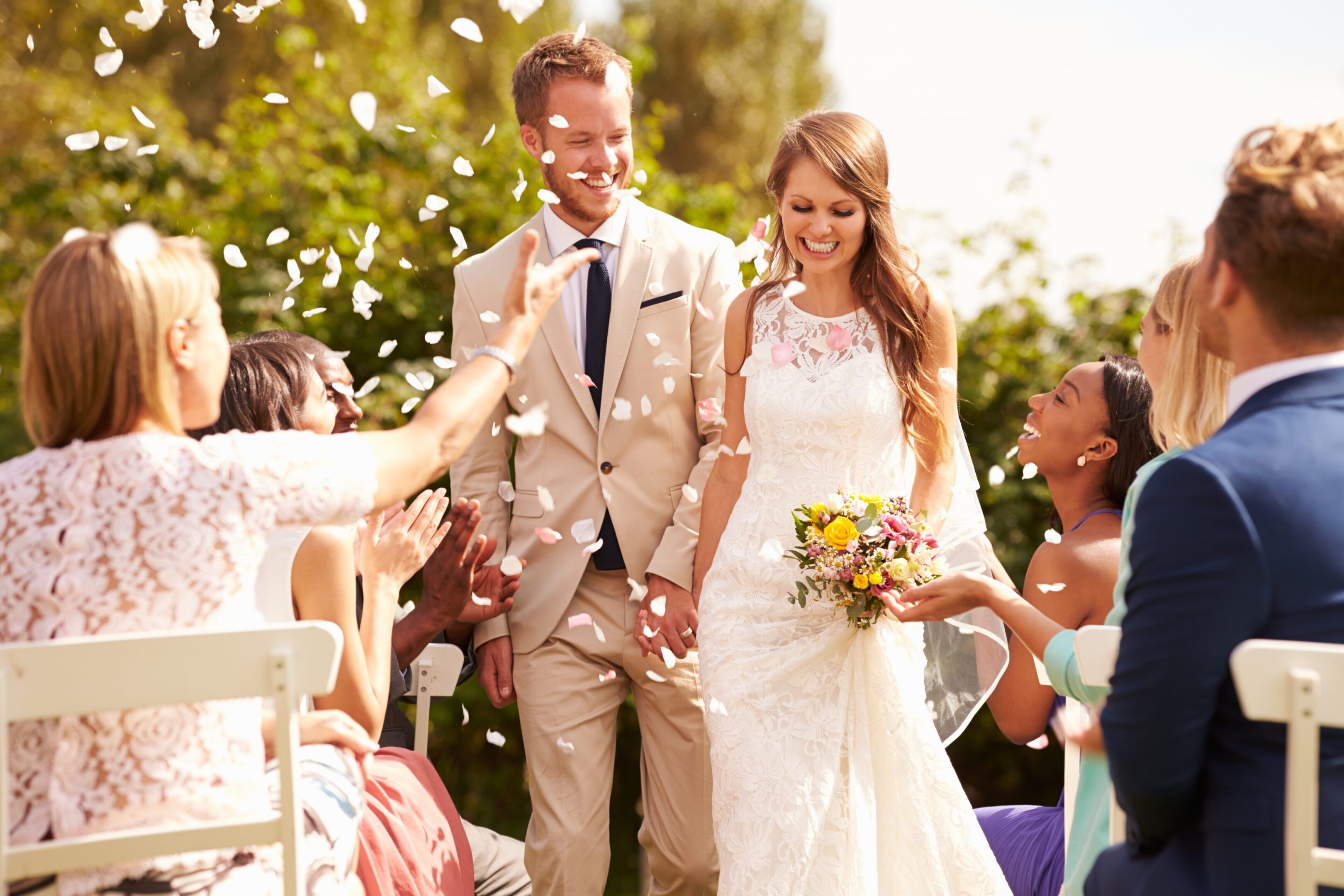 A bride and groom are standing outside with confetti.