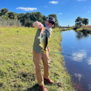 A man standing in the grass holding a fish.