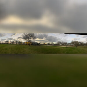 A view of a field with trees and clouds in the background.