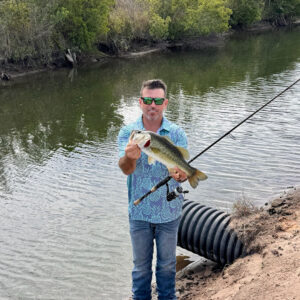 A man holding a fish while standing on the shore.