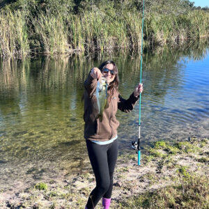 A woman standing on the shore of a lake holding a fish.