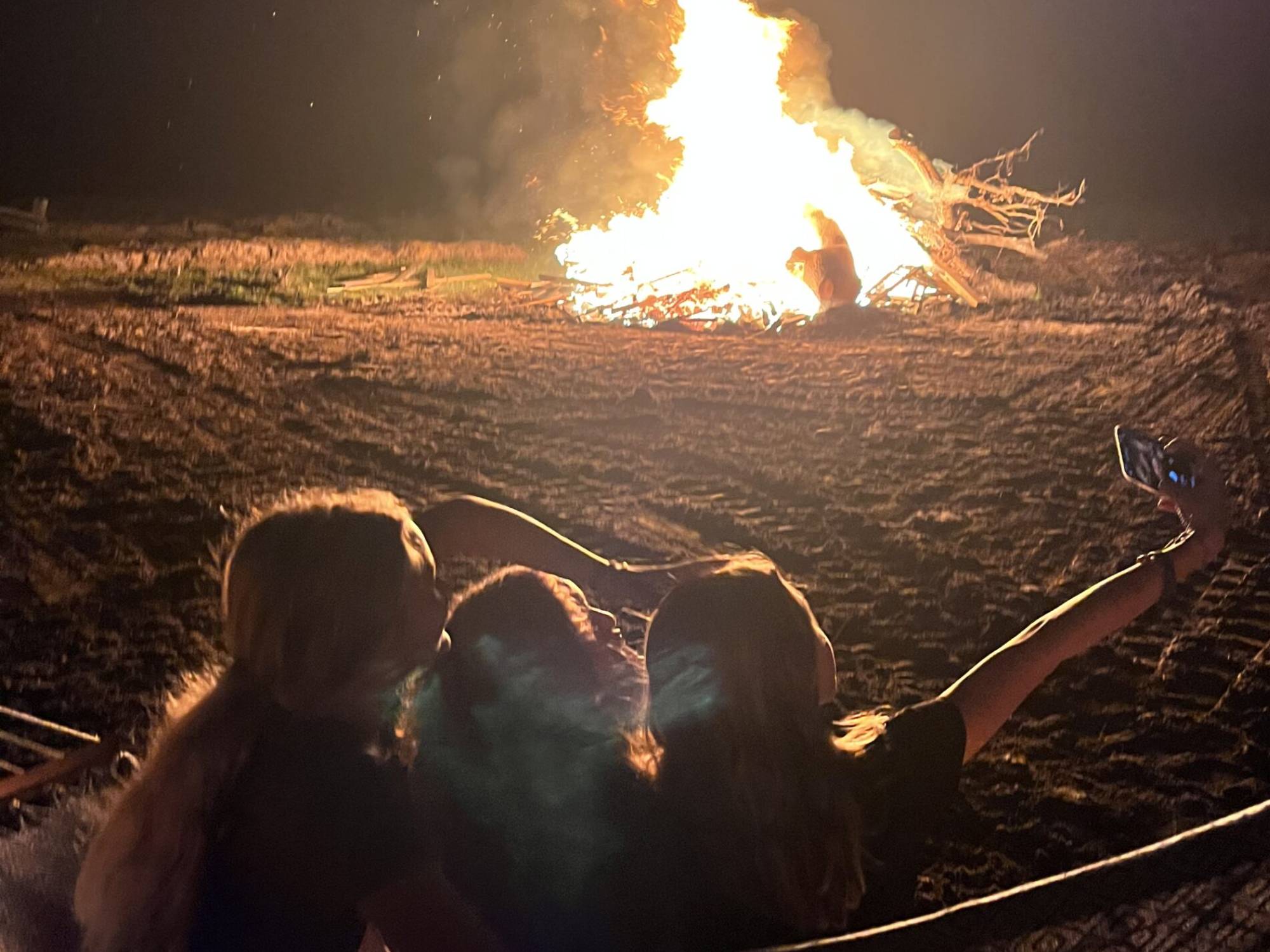 Three girls are sitting in the dirt near a fire.